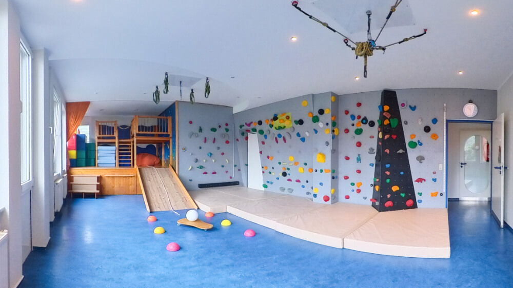 Großer, heller Therapieraum mit doppelter Kletterwand und mehreren Schaukeln